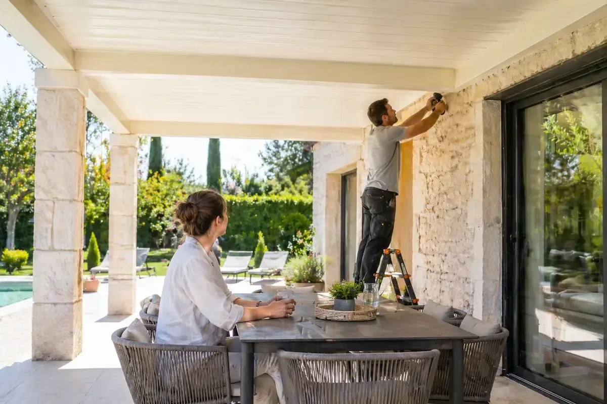 Terrasse couverte attenante à une maison, avec toiture prolongée, poteaux et mobilier de jardin